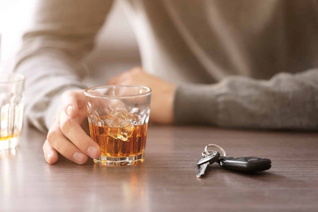 A person drinking with a pair of keys in front of them. If they drink and drive, they may face harsh Arizona DUI penalties