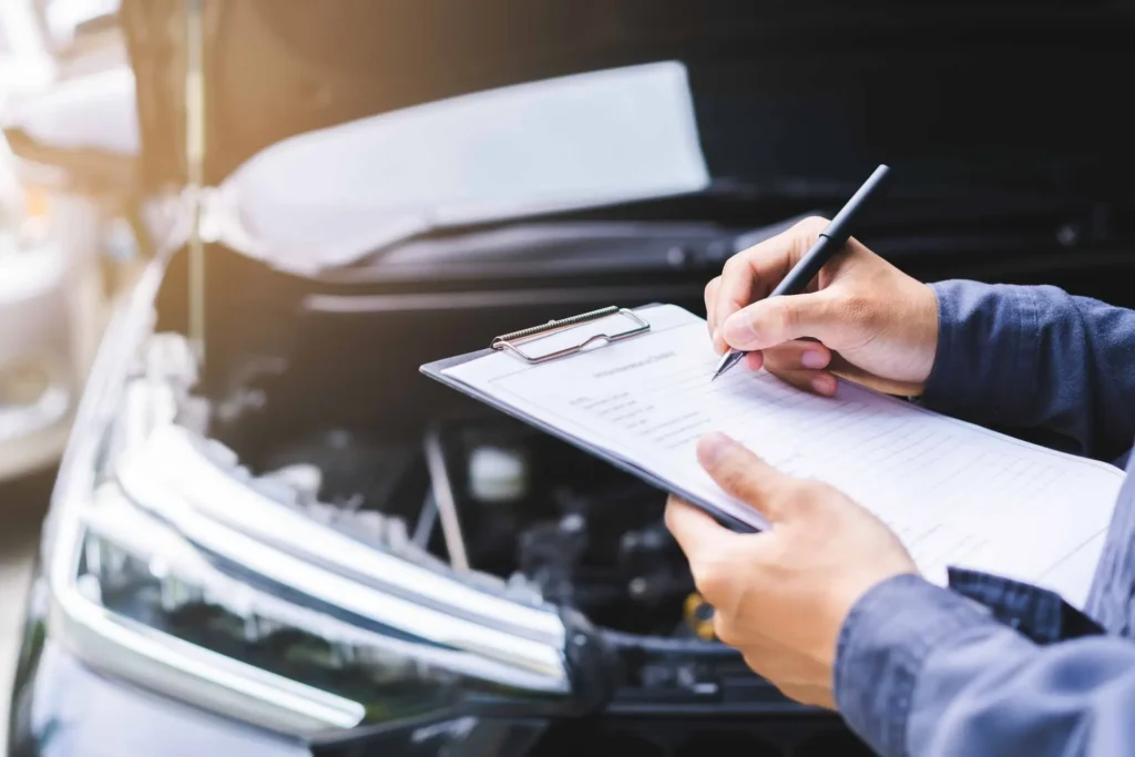 The concept of auto check-ups and car service shops is being discussed. Automobile repairman writing job checklist on clipboard, mechanic checking engine to estimate repair machine, inspecting maintenance by engineer at vehicle garage