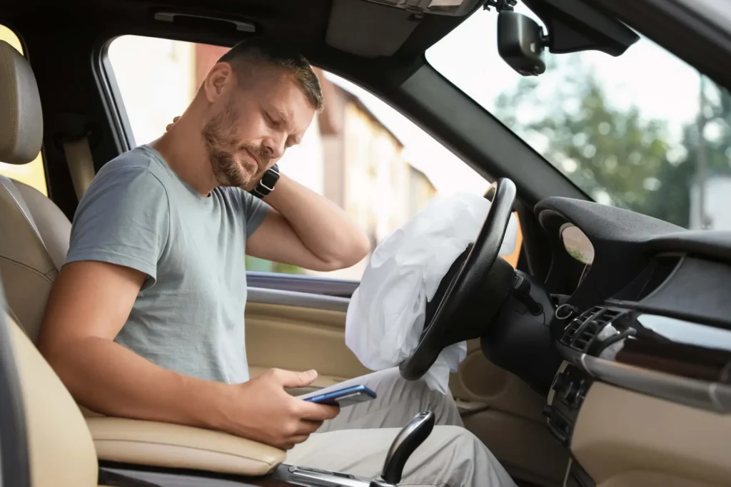 Man in a car looking at his phone after an airbag deployment
