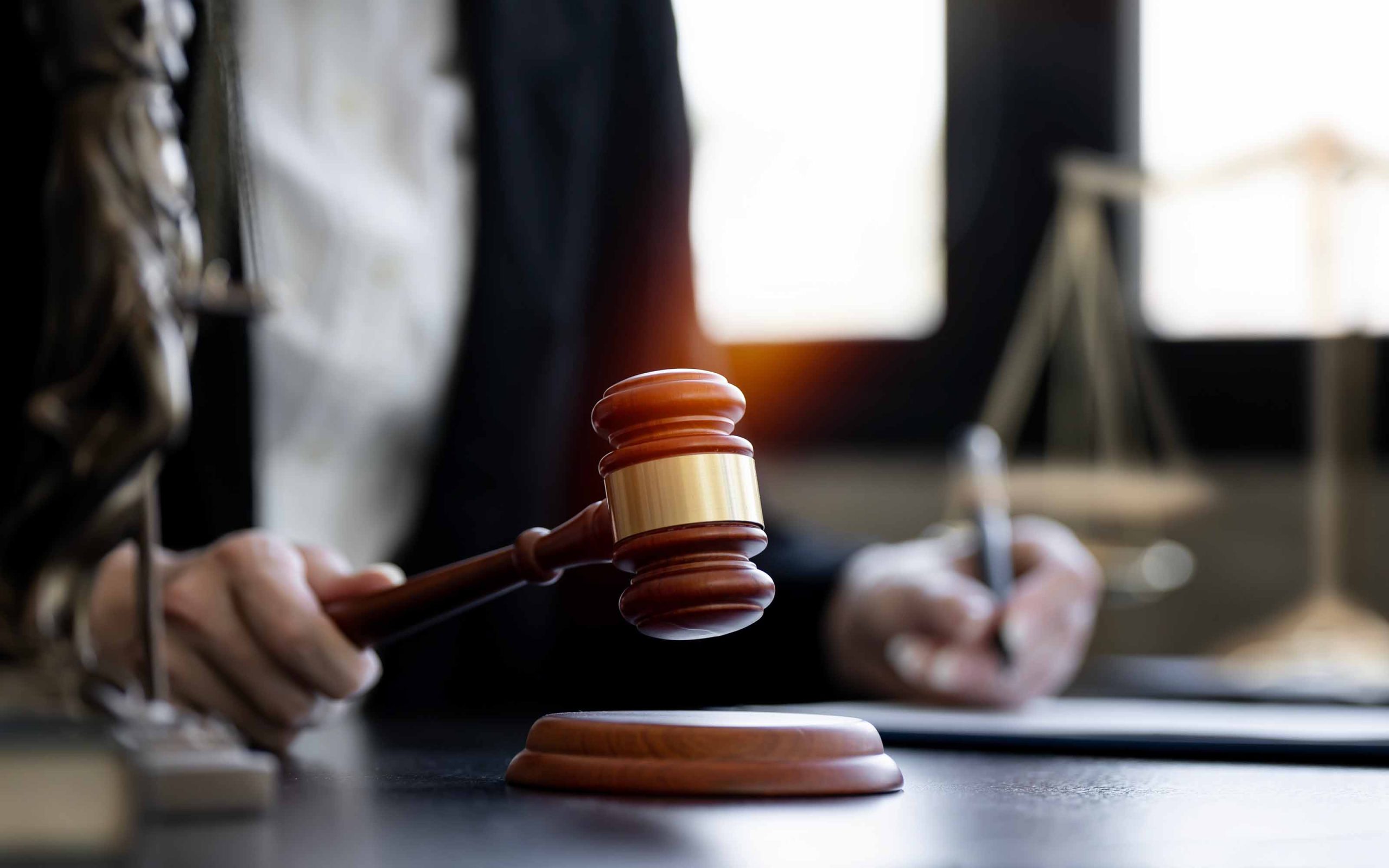 Judge holding a gavel in courtroom with legal documents and scales of justice in background