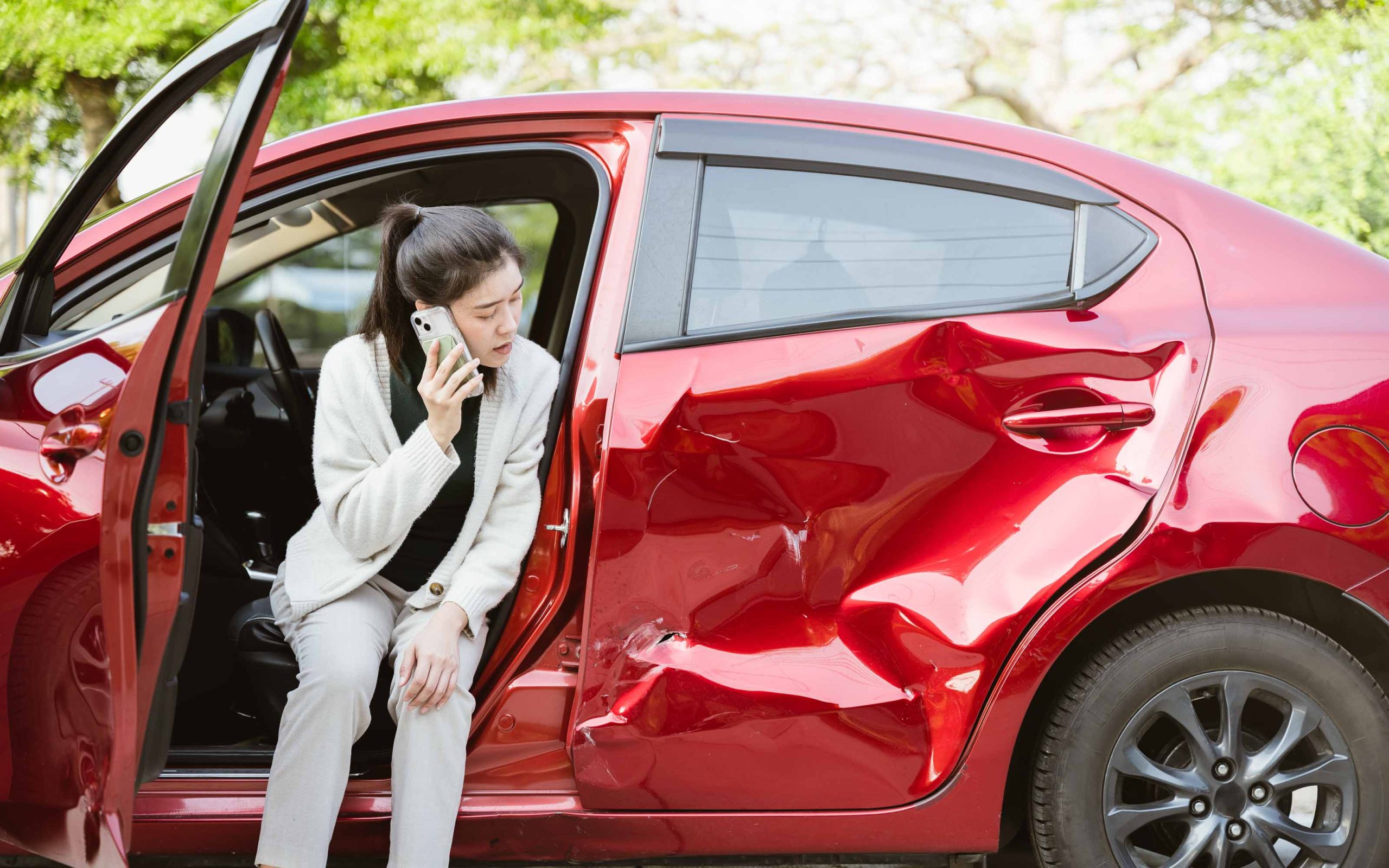Woman sitting in a damaged red car while calling for help after a side-impact accident.