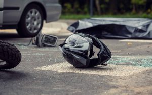 Motorcycle accident scene showing a damaged helmet on the road near a car and broken glass.