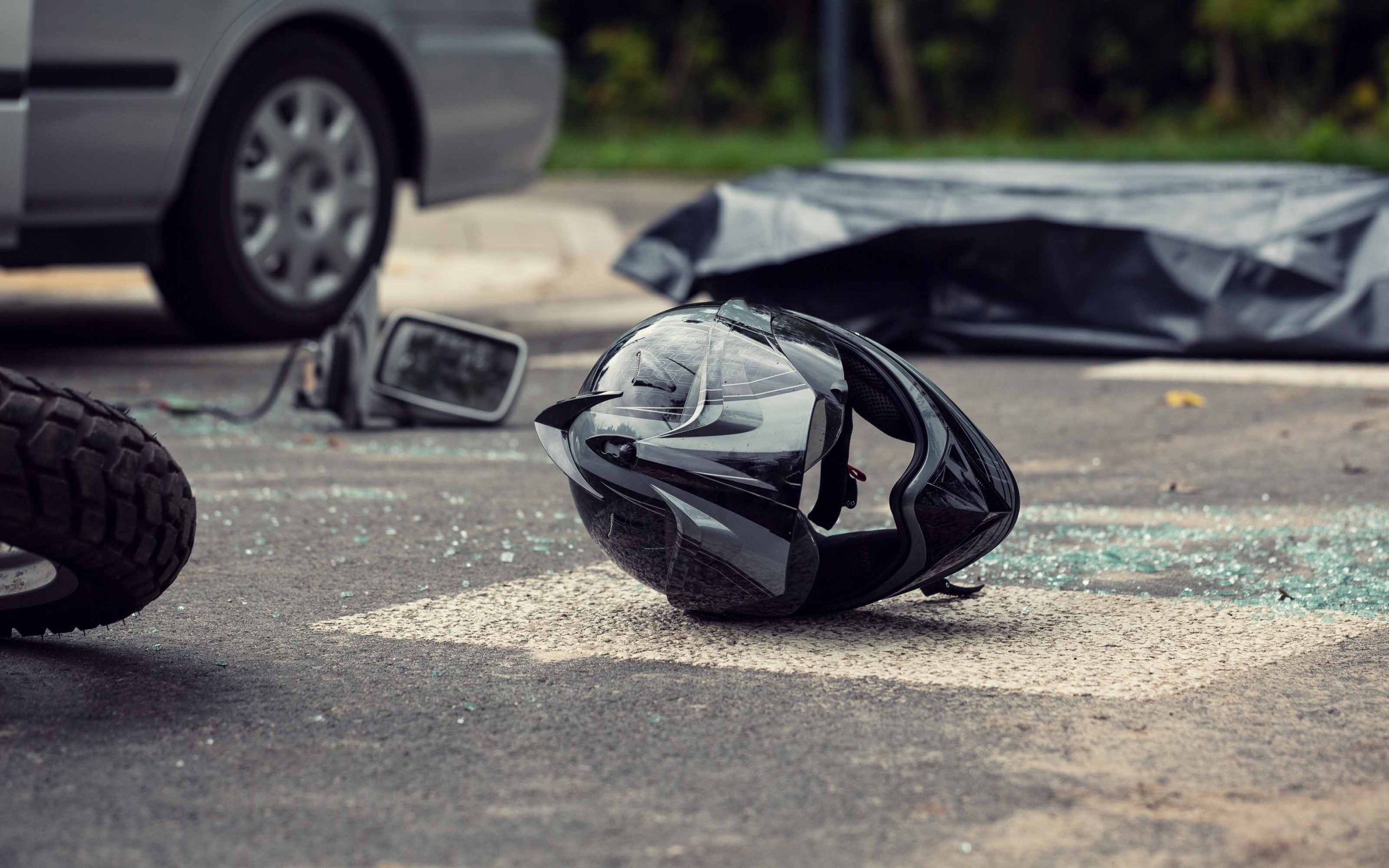 Motorcycle accident scene showing a damaged helmet on the road near a car and broken glass.