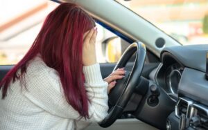 Woman with red hair sitting in a car, visibly distressed, holding her head in her hands, reflecting the emotional impact of car accidents involving uninsured drivers in Arizona.