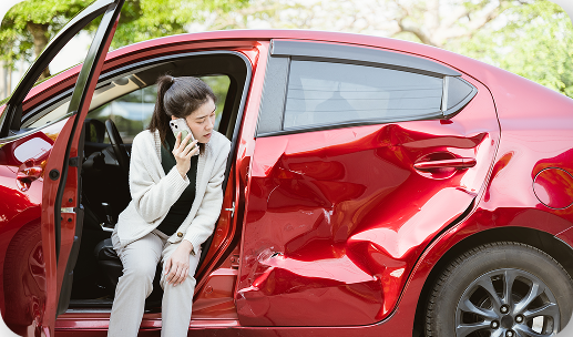 Woman on phone next to damaged red car after car accident in Tucson, Arizona.