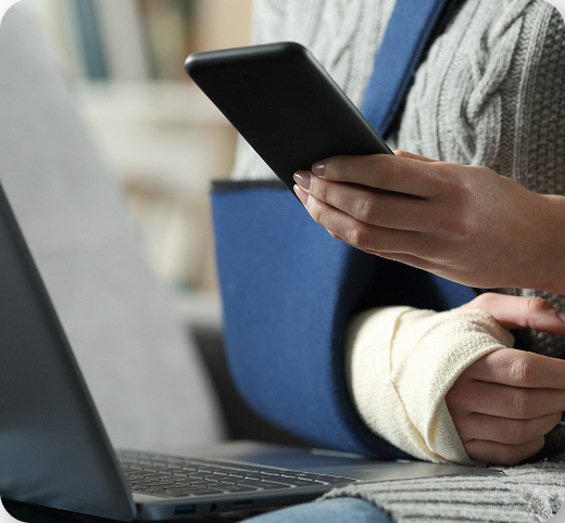 Injured person with arm sling using laptop and smartphone for injury claims in Tucson, Arizona.
