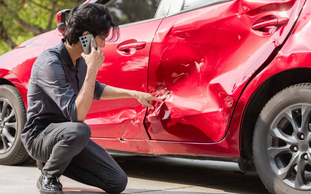 wreck red car with a person beside calling on phone