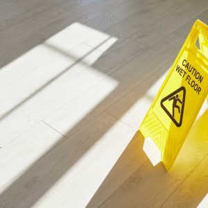 Yellow caution wet floor sign placed on light wooden flooring in sunlight.