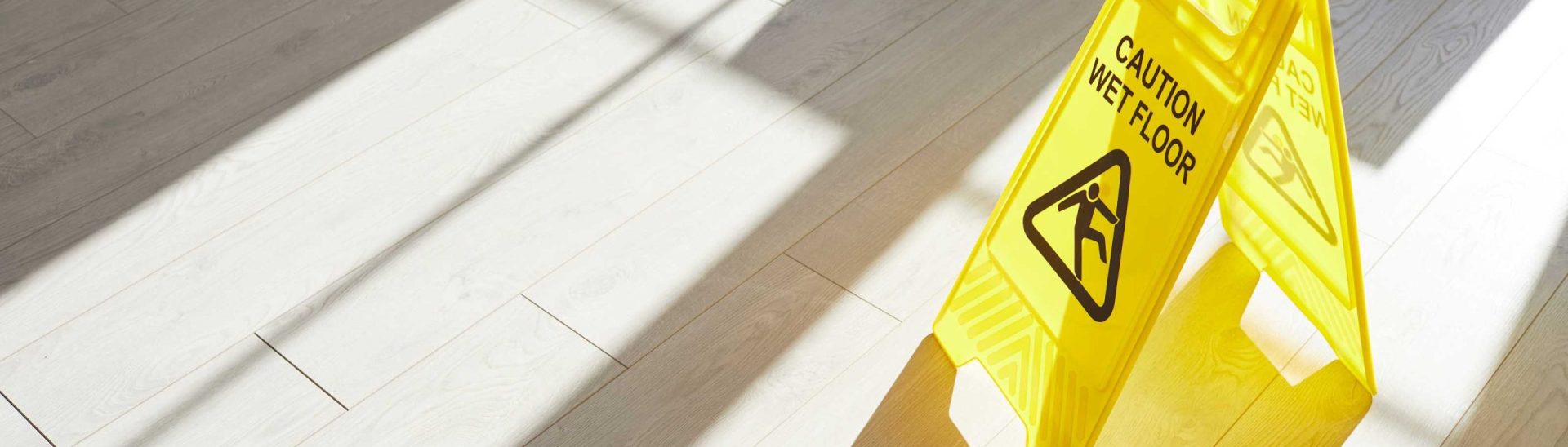 Caution wet floor sign on light-colored wooden flooring, emphasizing slip and fall hazards related to personal injury claims.