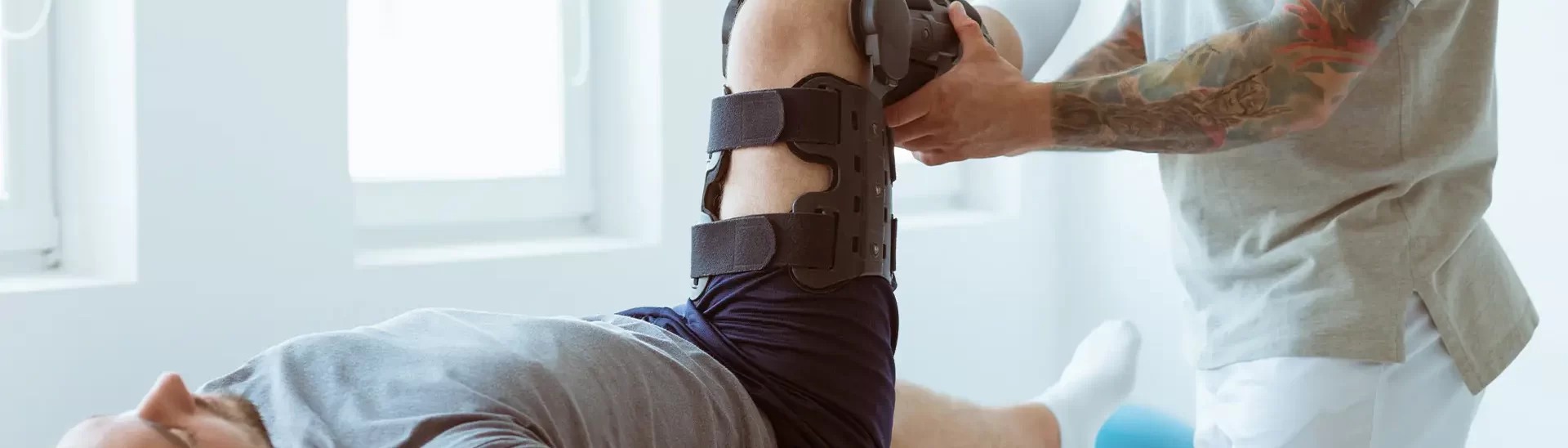 a man on a medical table with a knee brace adjusted by a healthcare professional in a bright clinic