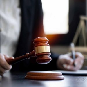 Judge holding a gavel in courtroom with legal documents and scales of justice in background