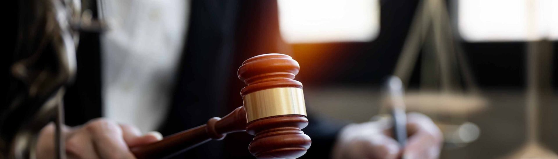 Judge holding a gavel in courtroom with legal documents and scales of justice in background
