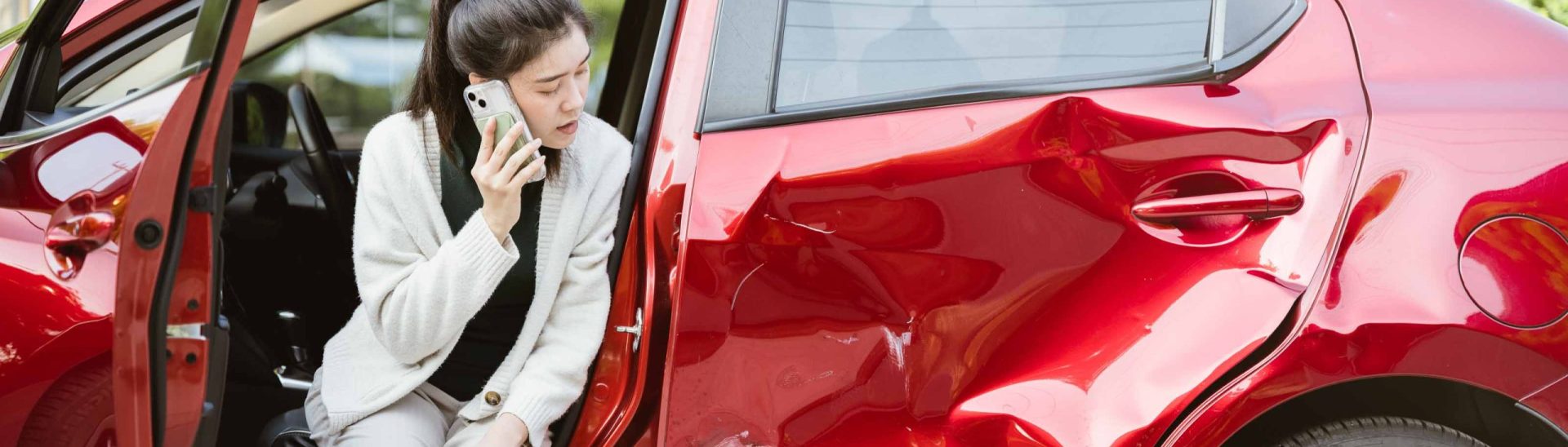 Woman sitting in a damaged red car while calling for help after a side-impact accident.