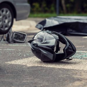 Motorcycle accident scene showing a damaged helmet on the road near a car and broken glass.