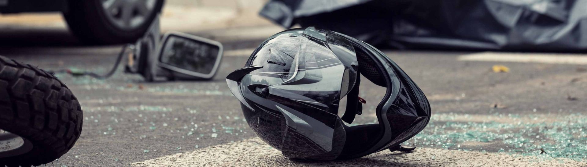 Motorcycle accident scene showing a damaged helmet on the road near a car and broken glass.