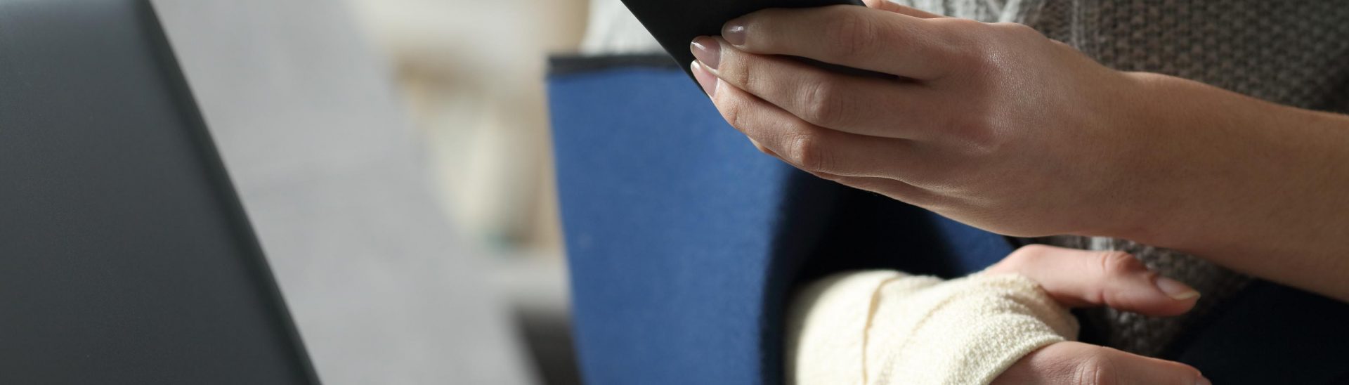 Close up portrait of a disabled woman with broken arm and sling using smartphone and laptop at home
