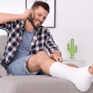 Man with broken leg in cast talking on mobile phone while sitting in armchair at home