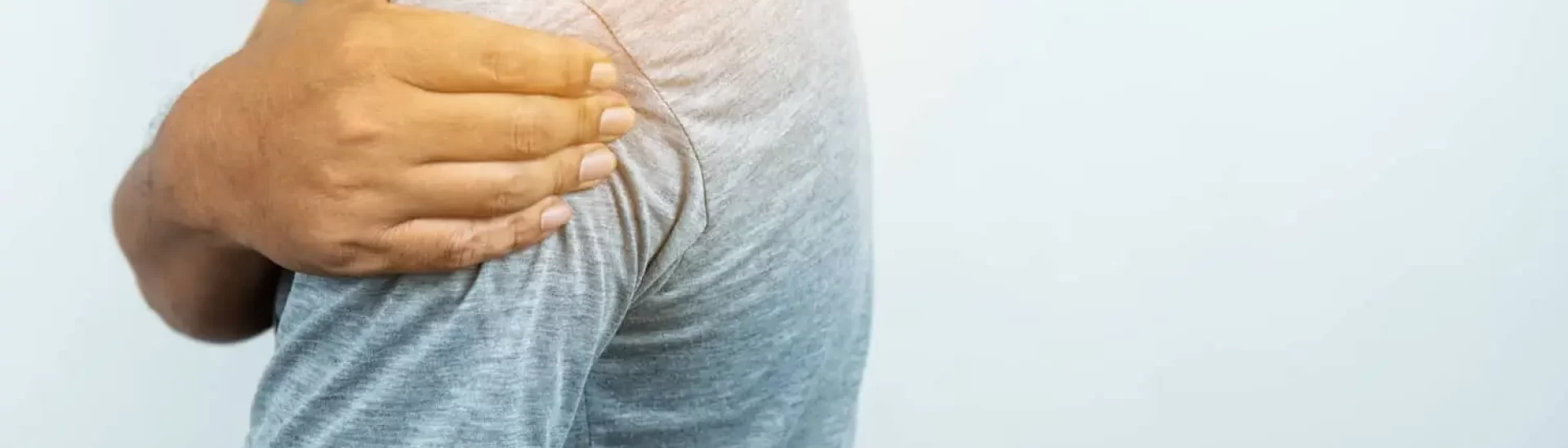 Person touching their shoulder, symbolizing discomfort or injury, relevant to discussions on Erb's palsy and its impact on mobility and physical health.