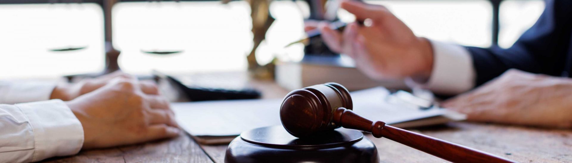 Close-up of a gavel on a wooden desk, with hands of two individuals discussing legal documents, emphasizing personal injury law and legal representation.
