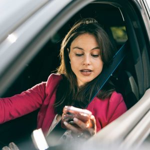 Young woman looking at mobile phone while driving her car.