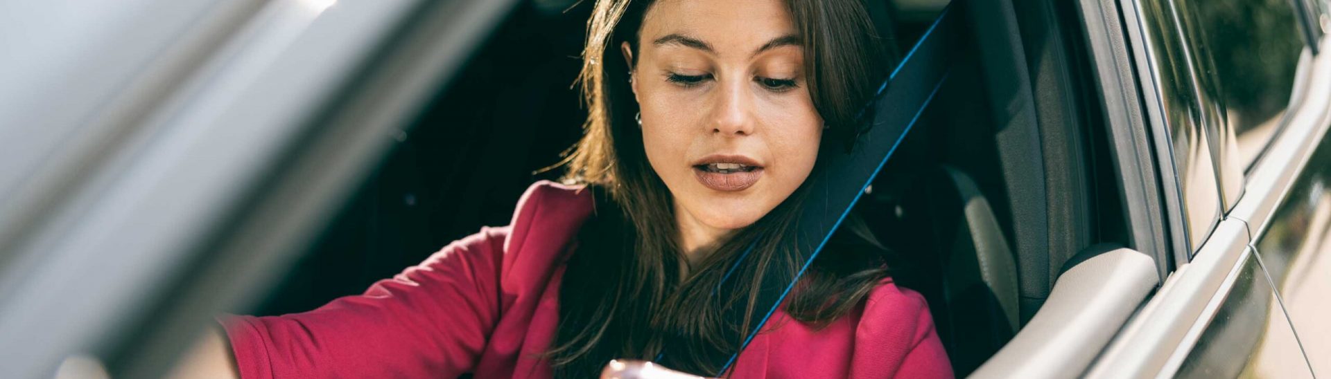Young woman looking at mobile phone while driving her car.