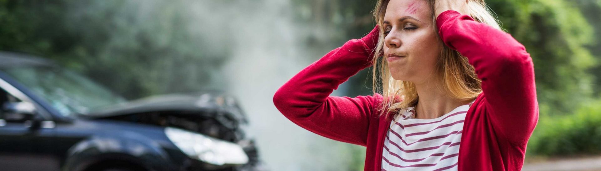 An injured young woman standing by the damaged car after a car accident.