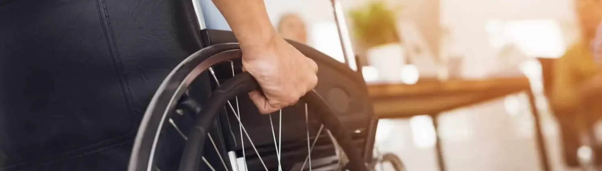 Close-up of a person’s hand on a wheelchair wheel, symbolizing mobility assistance and disability support.