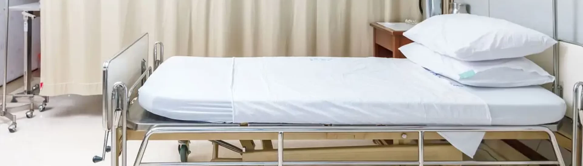 Empty hospital bed with white linens and pillows in a clean medical room, ready for the next patient.