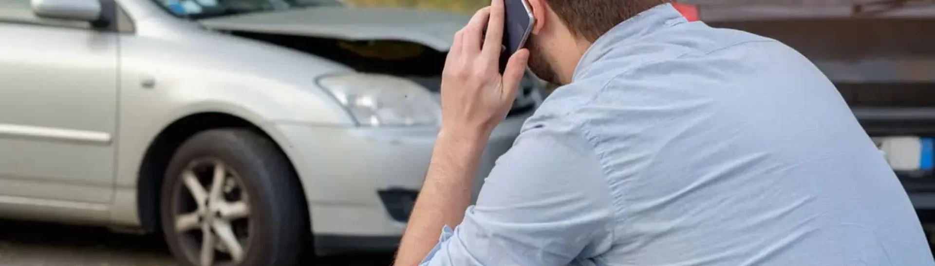 Man on phone near damaged car, representing steps to take after a road accident and the importance of legal assistance from Grabb & Durando.