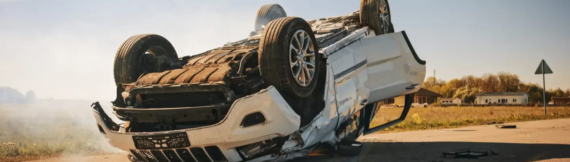 White SUV flipped upside down after a rollover accident on a rural road, showing extensive undercarriage damage.