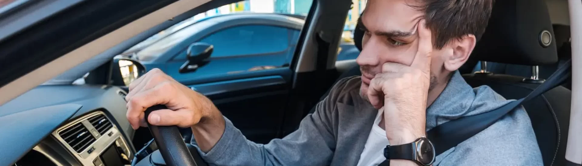 Frustrated male driver stuck in traffic, resting his head on his hand while sitting in a car.