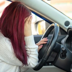 Woman with red hair holding her head in distress while sitting in a car, reflecting emotional impact of car accidents involving uninsured drivers in Arizona.