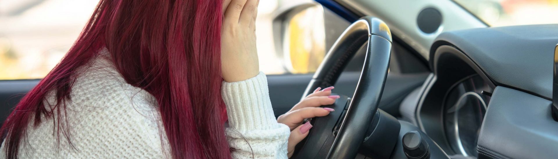 Woman behind the wheel of a car, holding her head: feeling unwell, accident